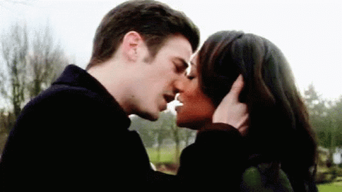 A Man And A Woman Are Kissing In Front Of Trees . GIF