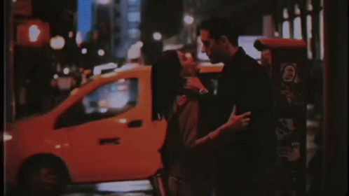 A Man And A Woman Are Kissing On A Street At Night . GIF