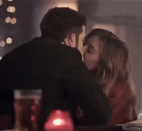 A Man And A Woman Are Kissing While Sitting At A Table In A Restaurant . GIF