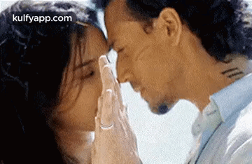 A Man And A Woman Are Kissing With Their Hands On Their Foreheads . GIF