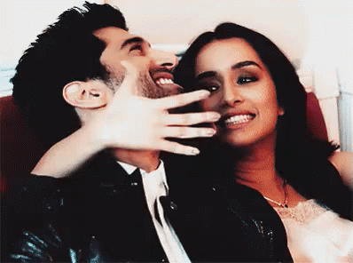 A Man And A Woman Are Laughing Together And The Woman Is Covering The Man 'S Mouth GIF