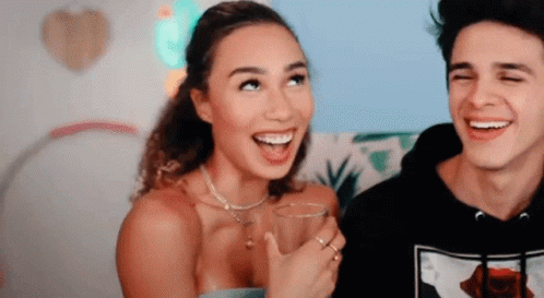 A Man And A Woman Are Laughing Together And The Woman Is Holding A Glass Of Water . GIF