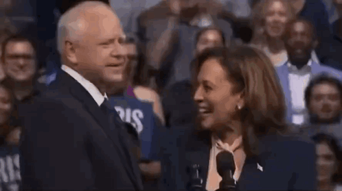 A Man And A Woman Are Laughing Together In Front Of A Crowd Of People . GIF