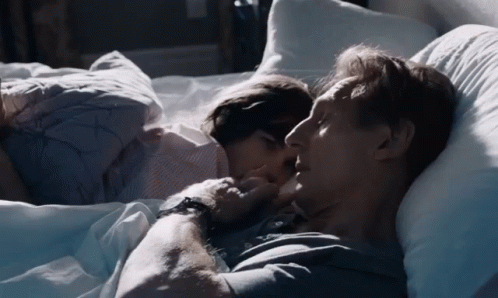 A Man And A Woman Are Laying In Bed And The Woman Is Kissing The Man 'S Neck GIF