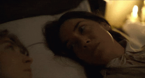 A Man And A Woman Are Laying In Bed And The Woman Is Looking At The Camera GIF