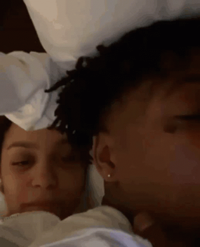 A Man And A Woman Are Laying In Bed With Their Eyes Closed . The Woman Is Wearing Earrings . GIF