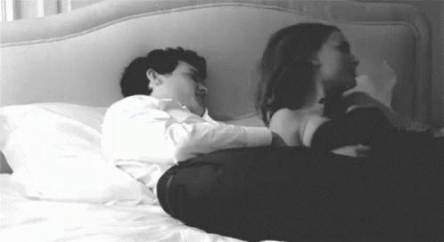 A Man And A Woman Are Laying On A Bed And Hugging Each Other . GIF