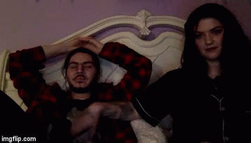 A Man And A Woman Are Laying On A Bed And The Man Has A Tattoo On His Arm GIF
