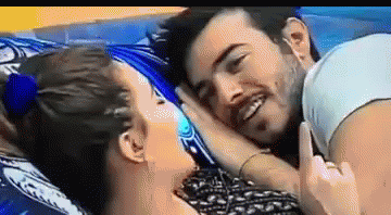 A Man And A Woman Are Laying On A Bed And The Woman Is Pointing At The Man 'S Face . GIF