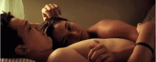 A Man And A Woman Are Laying On A Bed , The Woman Is Touching The Man 'S Hair . GIF