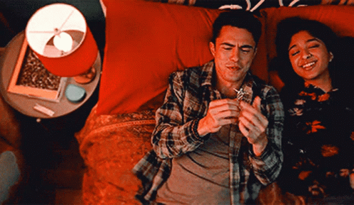A Man And A Woman Are Laying On A Bed With A Lamp In The Background GIF