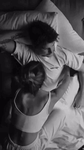 A Man And A Woman Are Laying On A Bed With Their Arms Around Each Other . GIF