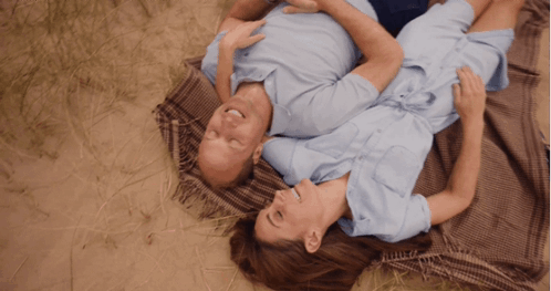 A Man And A Woman Are Laying On A Blanket In The Grass GIF