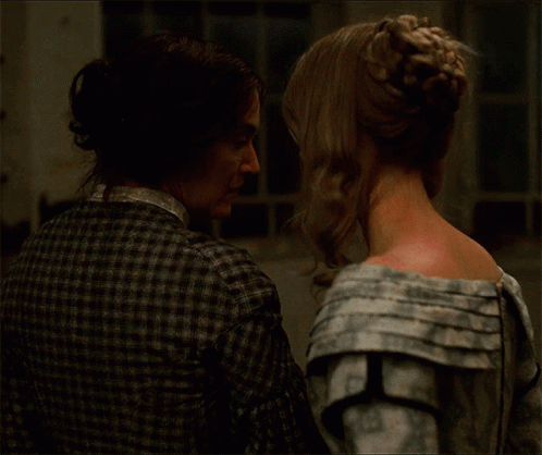 A Man And A Woman Are Looking At Each Other And The Woman Has A Bun In Her Hair GIF