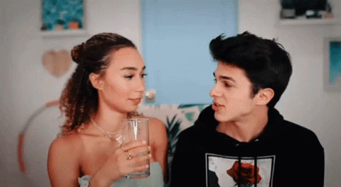 A Man And A Woman Are Looking At Each Other And The Woman Is Holding A Glass . GIF