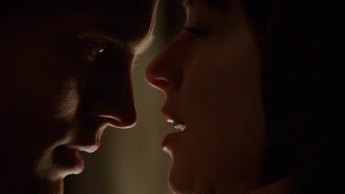A Man And A Woman Are Looking At Each Other In A Dark Room GIF