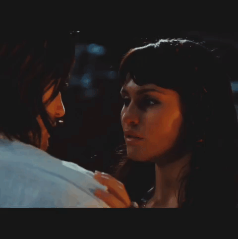 A Man And A Woman Are Looking At Each Other In A Dark Room GIF