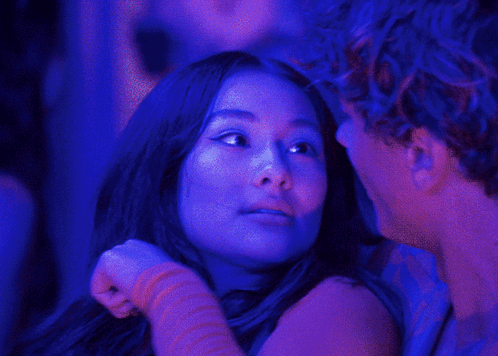 A Man And A Woman Are Looking At Each Other In A Dark Room With Blue Lights GIF