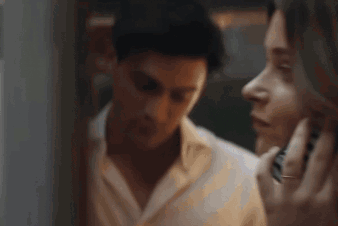 A Man And A Woman Are Looking At Each Other In A Mirror . The Man Is Covering His Ears With His Hand . GIF