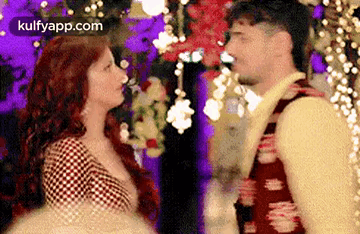 A Man And A Woman Are Looking At Each Other In A Room With Flowers In The Background . GIF