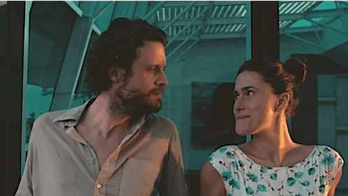 a man and a woman are looking at each other in front of a staircase