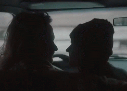 A Man And A Woman Are Looking At Each Other In The Back Seat Of A Car . GIF