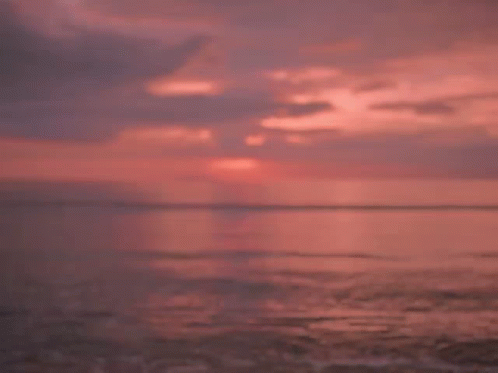 A Man And A Woman Are Looking At Each Other On A Beach At Sunset GIF