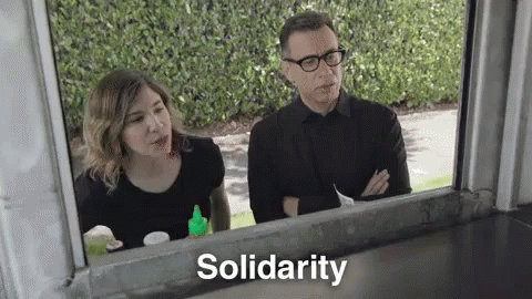 A Man And A Woman Are Looking Out Of A Window And The Word Solidarity Is Written On The Window . GIF
