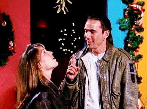 A Man And A Woman Are Looking Up At A Mistletoe GIF