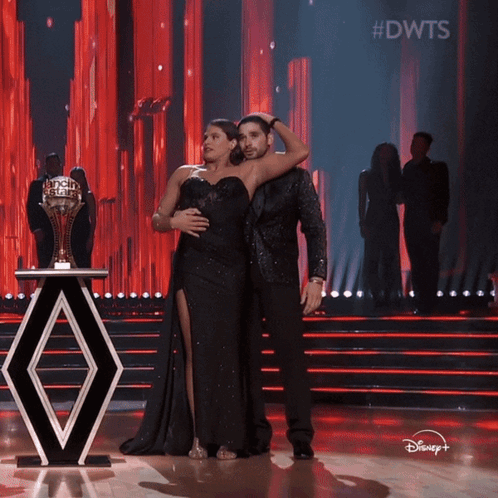 A Man And A Woman Are On A Stage With A Trophy In The Background And The Words #Dwts On The Bottom GIF