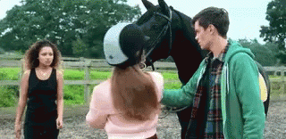 A Man And A Woman Are Petting A Horse In A Stable . GIF