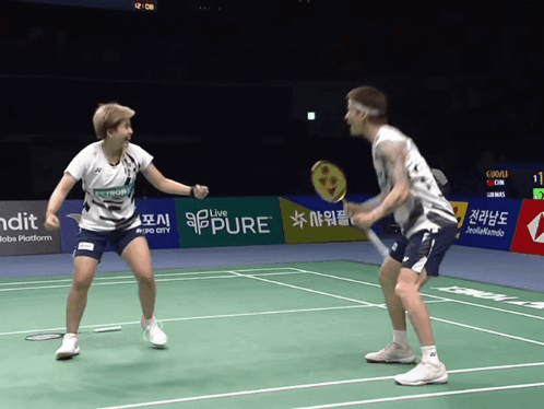 A Man And A Woman Are Playing A Game Of Badminton On A Court That Has A Banner That Says Pure GIF