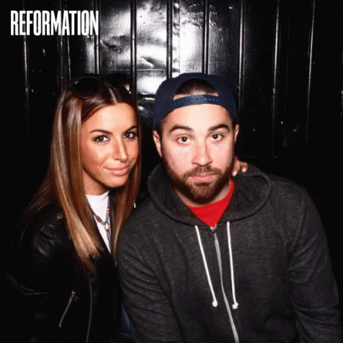 A Man And A Woman Are Posing For A Photo In Front Of A Wall That Says " Reformation " GIF
