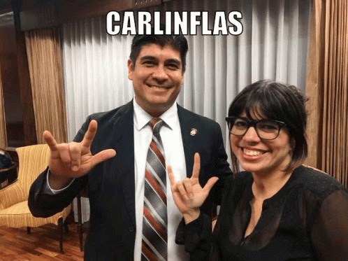 A Man And A Woman Are Posing For A Picture And The Man Is Wearing A Suit And Tie And The Woman Is Wearing Glasses GIF