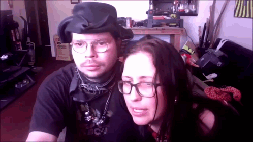 A Man And A Woman Are Posing For A Picture And The Woman Is Wearing Glasses And A Black Shirt That Says Bcj GIF