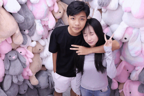a man and a woman are posing for a picture in front of a wall of stuffed animals