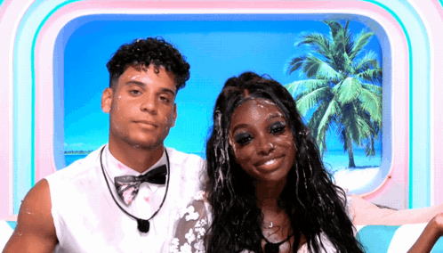 A Man And A Woman Are Posing For A Picture In Front Of A Window With Palm Trees In The Background GIF