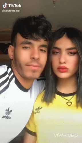 A Man And A Woman Are Posing For A Picture . The Woman Is Wearing A Yellow Adidas Shirt . GIF