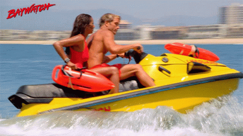 A Man And A Woman Are Riding A Yellow Jet Ski With Baywatch Written In Red GIF