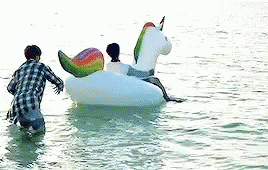 A Man And A Woman Are Riding On A Unicorn Float In The Water . GIF