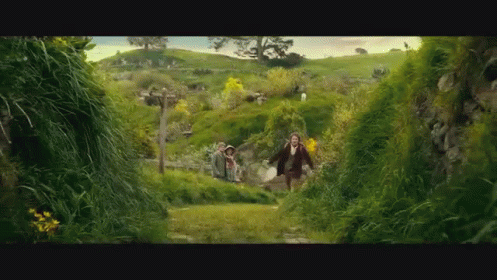 A Man And A Woman Are Running Through A Lush Green Field GIF