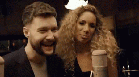 A Man And A Woman Are Singing Into A Microphone . GIF