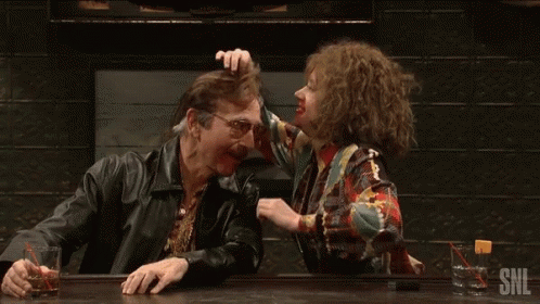 A Man And A Woman Are Sitting At A Bar And The Woman Is Touching The Man 'S Head . GIF