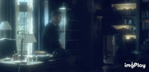 A Man And A Woman Are Sitting At A Desk In A Dark Room With The Words Imgplay Below Them GIF