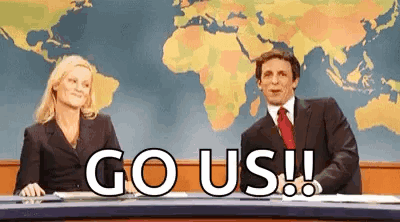A Man And A Woman Are Sitting At A News Desk With The Words `` Go Us '' Written In Front Of Them . GIF