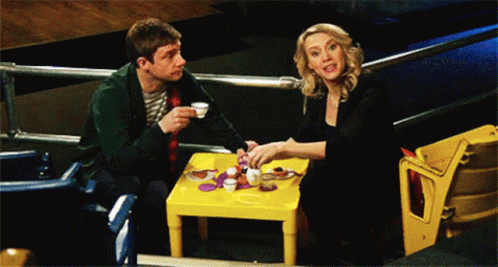 A Man And A Woman Are Sitting At A Small Table GIF