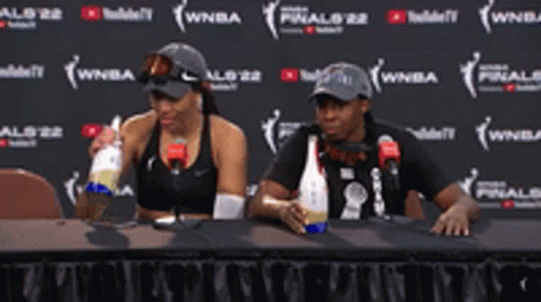 A Man And A Woman Are Sitting At A Table Drinking From Bottles GIF