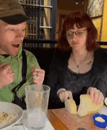 A Man And A Woman Are Sitting At A Table Eating Food And Drinking . GIF