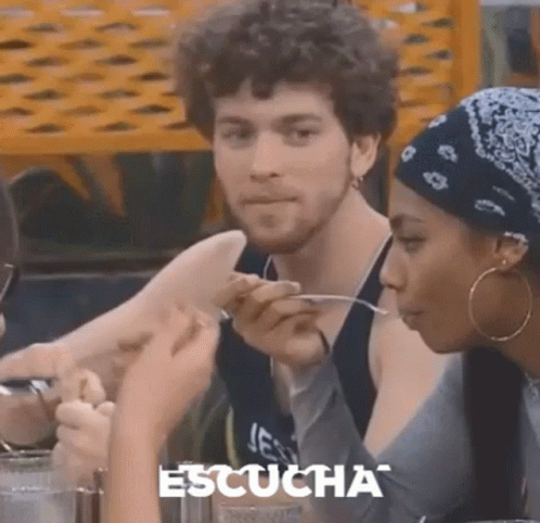 A Man And A Woman Are Sitting At A Table Eating Food With Spoons . GIF