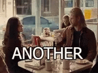 A Man And A Woman Are Sitting At A Table In A Diner With The Word Another Above Them . GIF